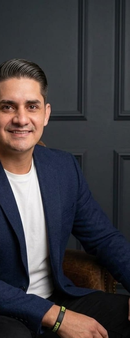 retrato profissional de um homem sorridente de blazer azul sentado numa poltrona de couro marrom com parede es
